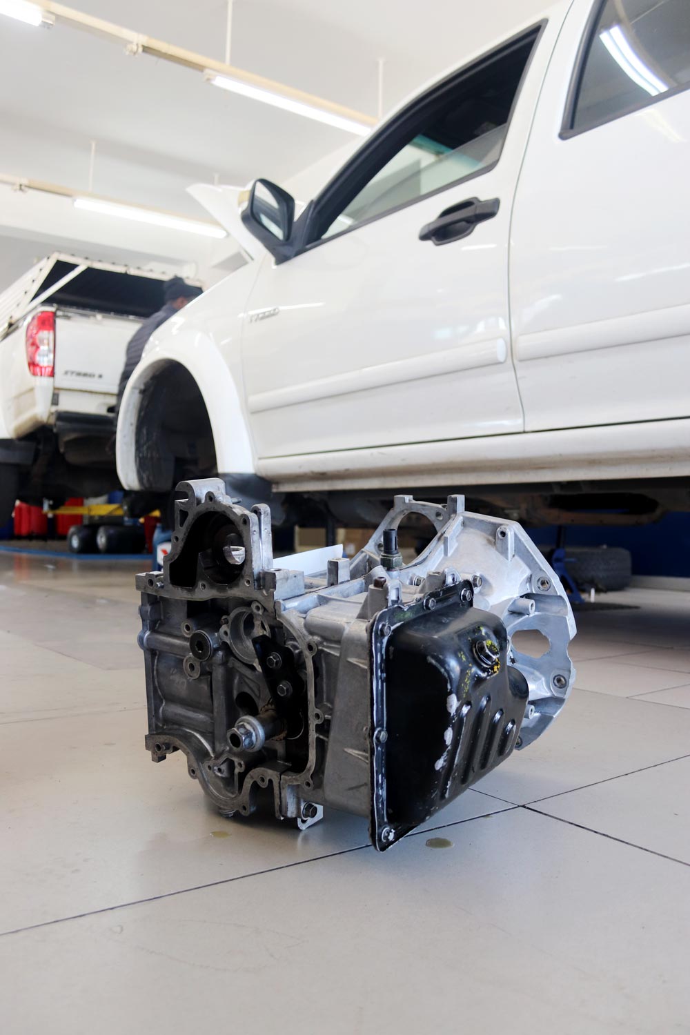 Removed gearbox on the workshop floor beside a bakkie on the lift